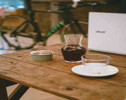A laptop on a clean wooden desk surrounded by a glass flask and a notebook