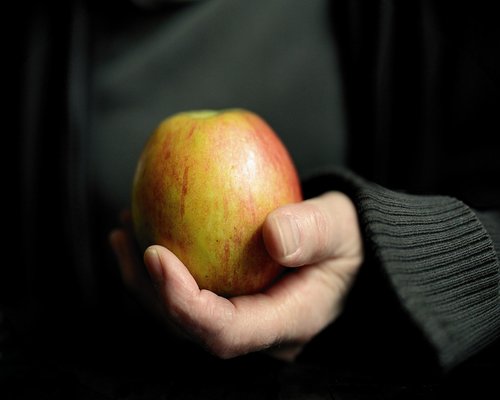A clear ceramic bowl filled with raw apples and nuts sitting on a bright domestic surface